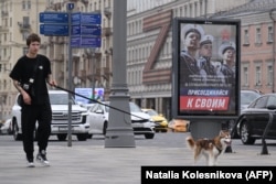 Молодой человек в центре Москвы выгуливает собаку на фоне плаката, пропагандирующего контрактную службу в армии РФ, с лозунгом "Присоединяйся к своим"